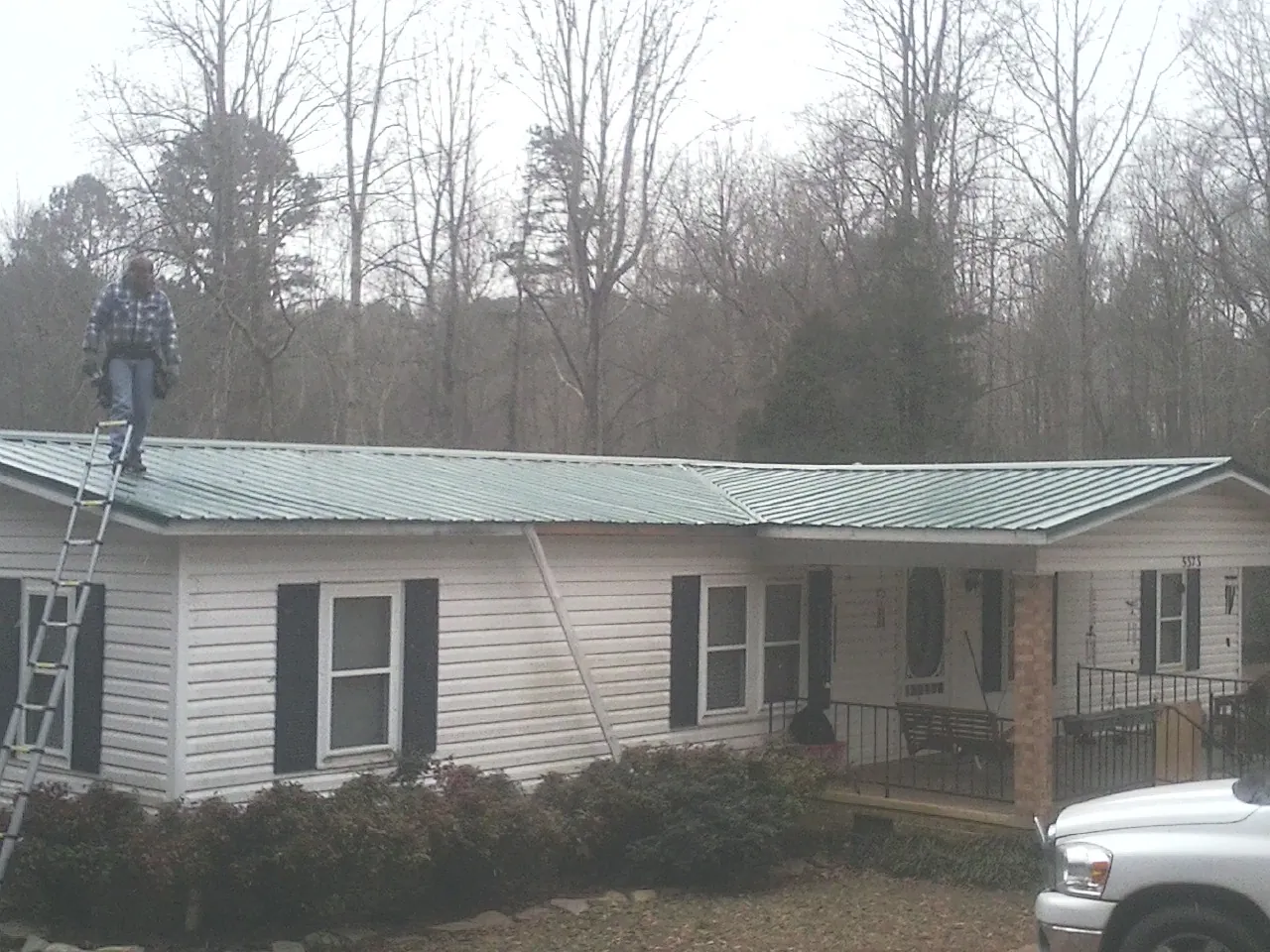 Worker on a ladder beside a new green metal roof on a ranch home in Pompey