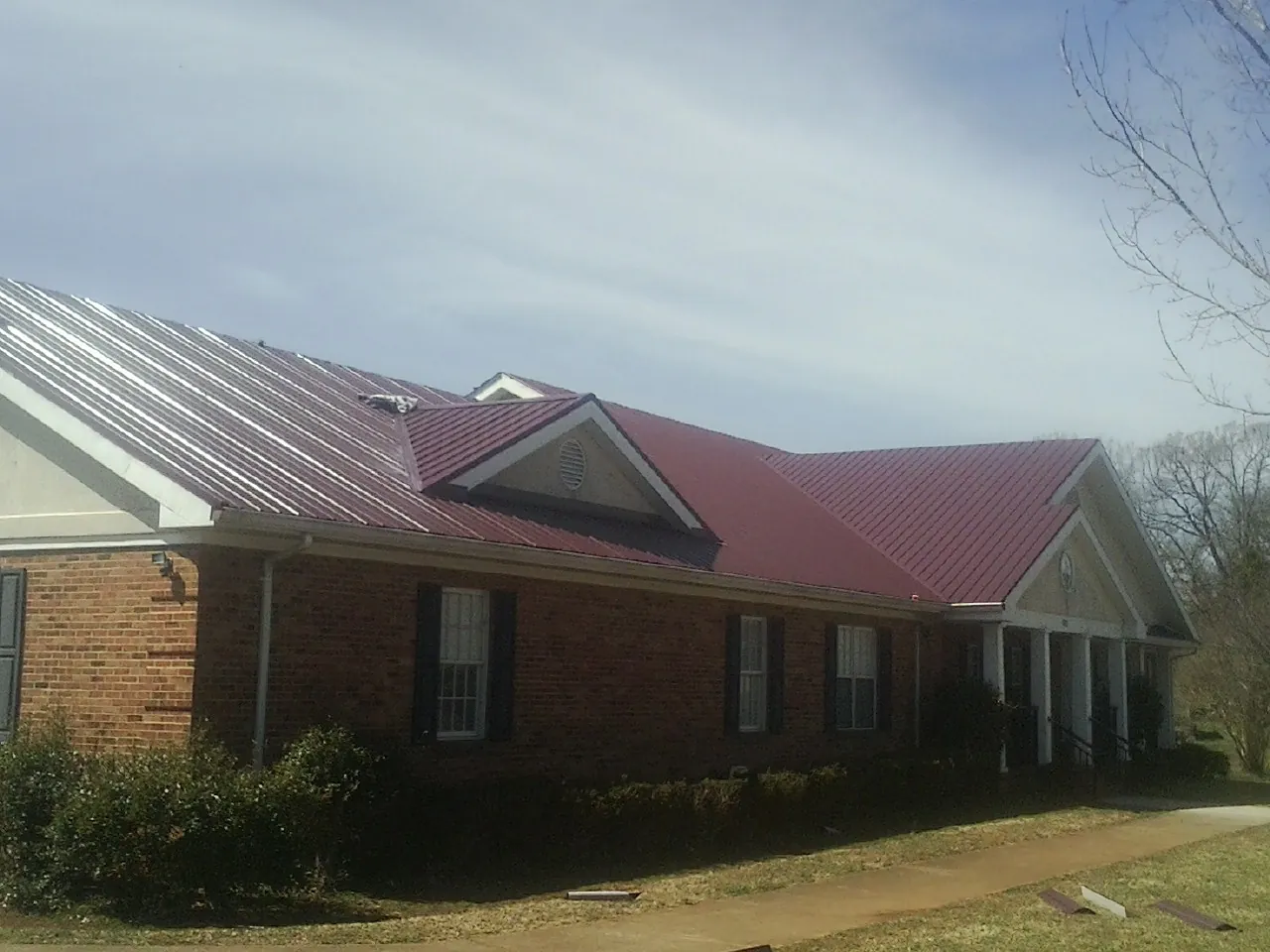 Red metal roof with gabled entries on a long brick building, from a Hail Damage Roof Repair job in Pompey