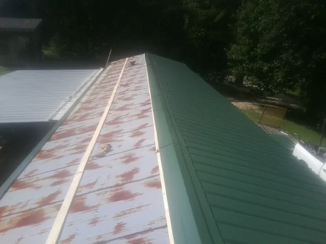 Old rusted panels beside newly installed green metal roofing — Wind Damage Roof Repair by Roofing Brothers in Pompey