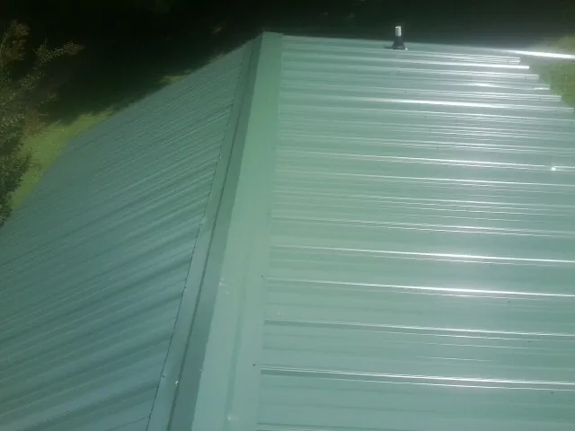 New green metal panels meeting at the ridge of a roof — Flat Roof Repair work by our crew in Pompey