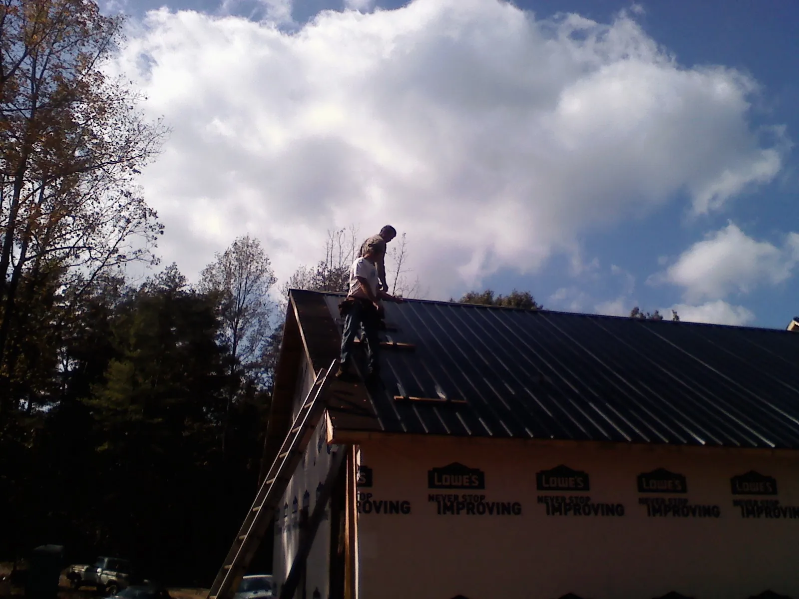 Roofer fastening dark metal panels high against a cloudy sky, from a Roof Inspection job in Pompey