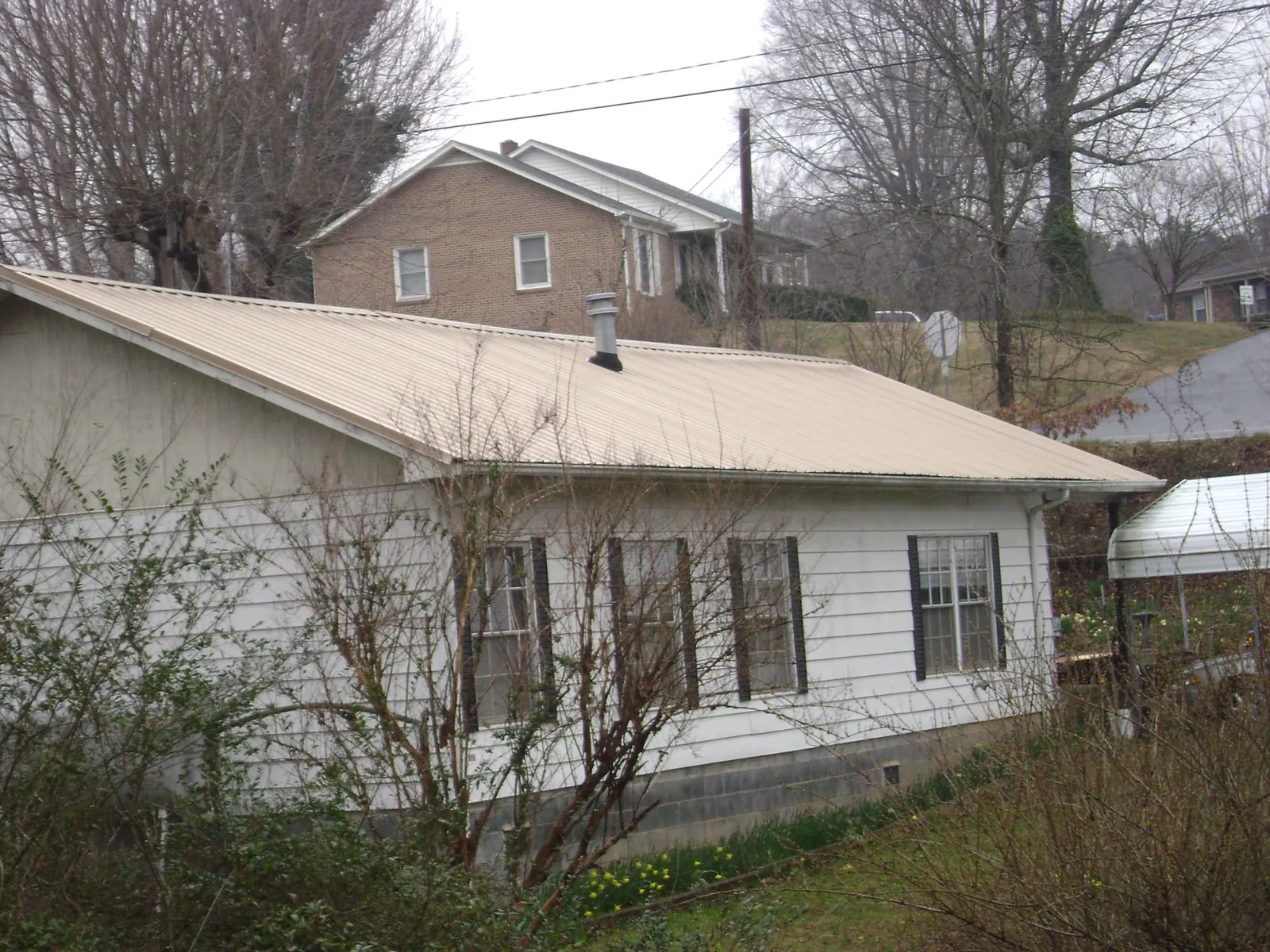 Tan metal roof on a white sided house set into a hillside — Commercial Roofing by Roofing Brothers in Pompey
