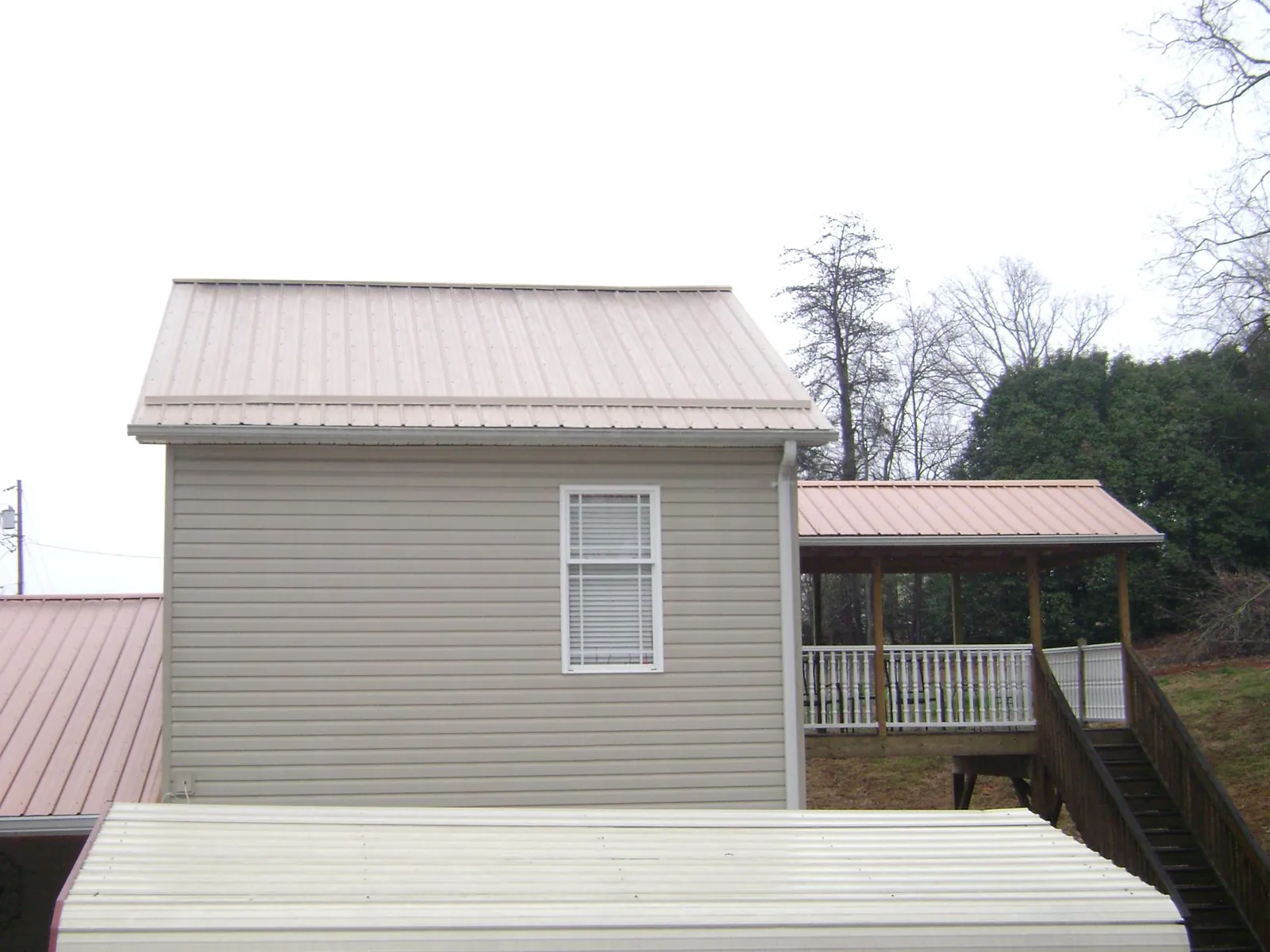 Tan metal roofs on a two story addition and attached porch, from a Roof Replacement job in Pompey